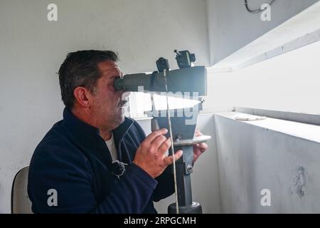 Un belvédère employé par des compagnies d'observation des baleines regarde à travers des jumelles alors qu'il regarde l'océan Atlantique pour des observations de baleines près d'Agua de Pau, île de Sao Miguel, Açores, Portugal. Les postes d'observation de la chasse à la baleine étaient autrefois utilisés par l'industrie baleinière pour chasser les baleines et font maintenant partie de l'éco-industrie d'observation des baleines, qui a connu un succès et est durable. Banque D'Images