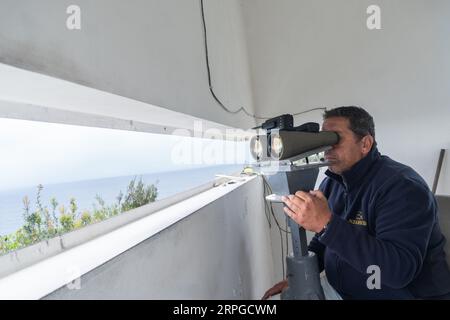 Un belvédère employé par des compagnies d'observation des baleines regarde à travers des jumelles alors qu'il regarde l'océan Atlantique pour des observations de baleines près d'Agua de Pau, île de Sao Miguel, Açores, Portugal. Les postes d'observation de la chasse à la baleine étaient autrefois utilisés par l'industrie baleinière pour chasser les baleines et font maintenant partie de l'éco-industrie d'observation des baleines, qui a connu un succès et est durable. Banque D'Images