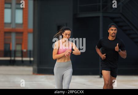 Deux athlètes sprintant sur un toit. Jeune femme vérifiant le tracker de fitness tout en courant. Banque D'Images