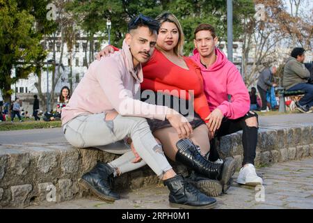 trois amis deux hommes de la communauté lgbt et une jeune femme de la taille du pus, latinos argentinos, assis dans le parc profitant du coucher du soleil ensemble. Banque D'Images