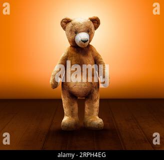 mignon ours en peluche se tient devant un mur orange et un plancher en bois Banque D'Images