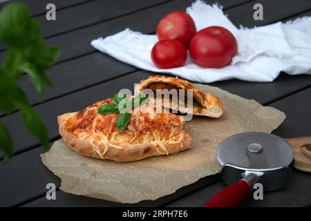 Pizza calzone découpée avec sauce tomate, pesto vert et fromage sur assiette en bois Banque D'Images