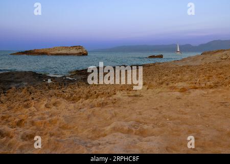 Assistez à la magie pure du lever du jour le long de la côte de Crète alors que le soleil commence son ascension. Un rivage rocheux se dresse fort au premier plan, tandis que deux Banque D'Images