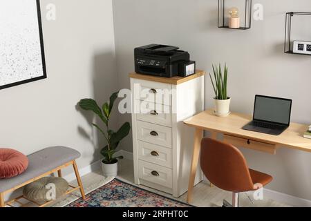 Imprimante moderne sur la commode près de la table en bois à l'intérieur Banque D'Images