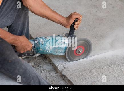 Un ouvrier coupe un plancher de béton avec une scie circulaire électrique sur un chantier de construction. Banque D'Images