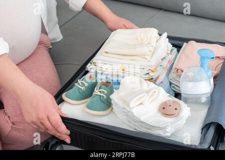Femme enceinte tenant des chaussures pour bébé et emballant le sac de maternité de l'hôpital. Mère pendant la grossesse attendant que bébé prépare une valise de vêtements, de jouets et Banque D'Images