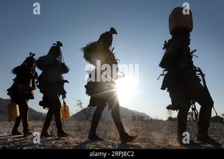 Les femmes Himba marchent toutes en une seule ligne tout en revenant de la collecte d'eau. L'eau est effrayante dans le nord de la Namibie, donc toutes les rations doivent être ramassées Banque D'Images