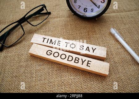 Un réveil, des lunettes, un stylo et des blocs de bois qui disent le temps de dire au revoir! sur fond de toile de jute. Banque D'Images