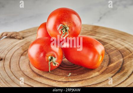 Tomates prune empilées dans la colline sur un fond en bois sur marbre blanc Banque D'Images