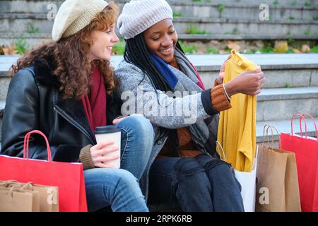 Deux amies multiraciales à la recherche des vêtements qu'elles ont achetés après avoir fait du shopping en hiver. Banque D'Images