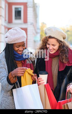 Deux amies multiraciales à la recherche des vêtements qu'elles ont achetés après avoir fait du shopping en hiver. Banque D'Images