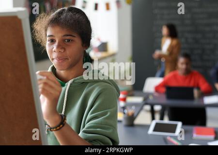 Écolière afro-américaine écrivant au tableau noir dans la salle de classe pendant la leçon Banque D'Images