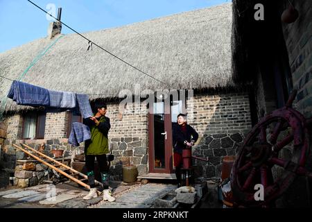 200115 -- RONGCHENG, le 15 janvier 2020 -- Yu Haiyang parle avec sa mère pendant qu'il suspend des draps dans le village de Yandunjiao à Rongcheng, dans la province du Shandong, dans l'est de la Chine, le 12 janvier 2020. Yandunjiao, un village côtier dans le Shandong, est plein de vitalité car de nombreux cygnes hivernent ici. À la fin de 2014, le service de train à grande vitesse entre Qingdao et Rongcheng a été lancé et de nombreux touristes sont venus ici pour voir des cygnes, déguster des spécialités locales et faire l'expérience d'un séjour chez l'habitant dans des maisons aux toits d'algues. Yu Haiyang, un villageois natif qui a travaillé à Singapour après l'obtention de son diplôme, est retourné dans sa ville natale et a commencé un séjour chez l'habitant Banque D'Images