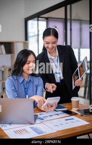 Deux femmes d'affaires asiatiques heureuses et professionnelles ou comptables ont une discussion sur leur projet financier, à l'aide d'une calculatrice, et WO Banque D'Images
