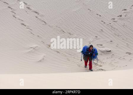 200116 -- XAYAR , 16 janvier 2020 -- Zhou Fuxiang portant des câbles marche sur une dune dans le désert de Taklimakan, dans la région autonome ouïgoure du Xinjiang, au nord-ouest de la Chine, 15 janvier 2020. Les travailleurs de l'exploration pétrolière de BGP Inc., China National Petroleum Corporation, dont plus de 60 femmes, travaillent dur dans le désert de Taklimakan. CHINE-XINJIANG-TAKLIMAKAN DESERT-OIL TRAVAILLEUR CN DINGXLEI PUBLICATIONXNOTXINXCHN Banque D'Images