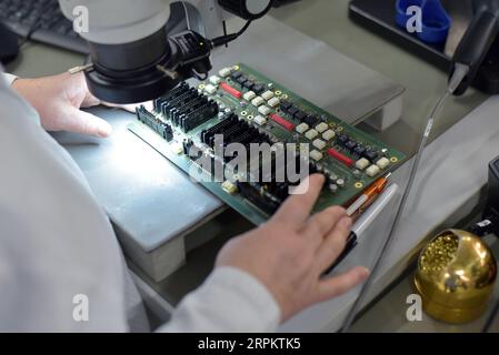 Femme dans une usine pour la production de composants électroniques vérifie la qualité d'un conseil assemblé avec l'aide d'un microscope ou une loupe gl Banque D'Images