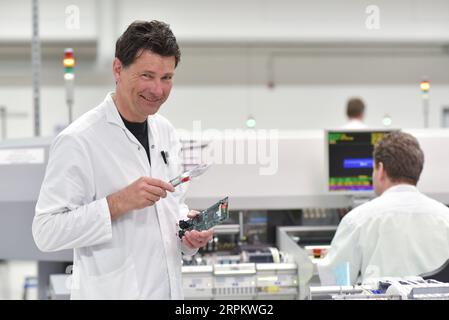 ingénieur dans une usine pour la production de composants électroniques vérifie la qualité d'une carte assemblée à l'aide d'une loupe Banque D'Images