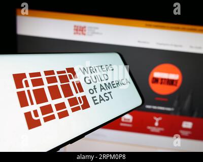 Smartphone avec le logo du syndicat Writers Guild of America East (WGAE) sur l'écran devant le site Web. Concentrez-vous sur le centre gauche de l'écran du téléphone. Banque D'Images