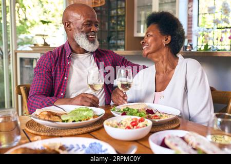 Couple senior amoureux assis autour de la table à la maison appréciant un repas avec vin ensemble Banque D'Images
