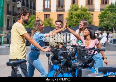Groupe d'amis multi-ethniques dans la ville à côté de vélos de location ayant du plaisir et high-fiving Banque D'Images