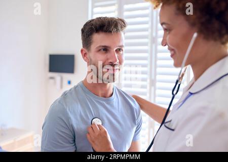 Infirmière féminine portant l'uniforme écoutant la poitrine du patient masculin dans la chambre d'hôpital privée Banque D'Images