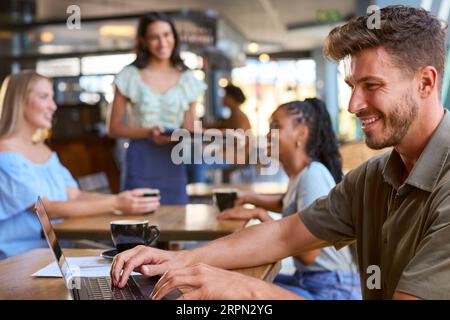 Homme travaillant sur un ordinateur portable assis à table dans un café-restaurant occupé Banque D'Images