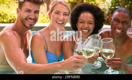 Portrait de Groupe d'amis multi-culturels souriants en vacances dans la piscine boire du vin Banque D'Images