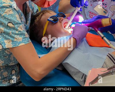 femme dentiste et infirmière traitant un patient de petit garçon avec un écarteur de lèvre et de joue sur sa bouche assis dans une chaise au cabinet dentaire Banque D'Images