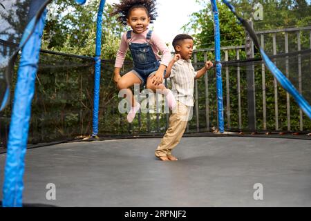 Garçon et fille ayant du plaisir à jouer dans le jardin rebondissant sur Trampoline Banque D'Images