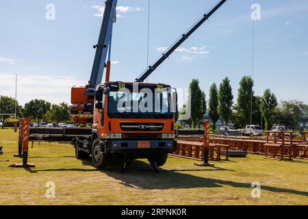 Une grue orange soulève un échafaudage métallique pour construire une scène pour un festival de musique Banque D'Images