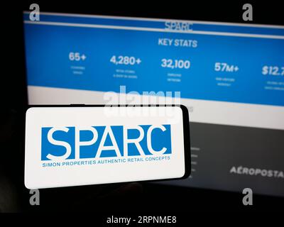 Personne tenant un téléphone portable avec le logo de la société de détail américaine SPARC Group LLC sur l'écran devant la page Web. Concentrez-vous sur l'affichage du téléphone. Banque D'Images