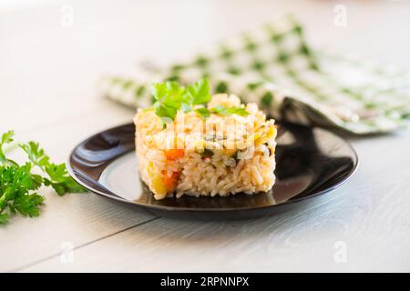 Riz bouilli cuit avec des courgettes, des carottes et des légumes dans une assiette, sur une table en bois clair. Banque D'Images