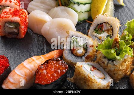 Sushi set de rouleaux avec coquilles Saint-Jacques et légumes, sur pierre noire Banque D'Images