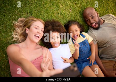 Vue aérienne de la famille multi-raciale couchée sur l'herbe prenant Selfie sur le téléphone portable Banque D'Images