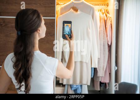 Jeune femme prenant des photos de vieux vêtements indésirables à vendre dans l'application smartphone Banque D'Images