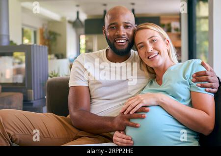 Aimer couple multi-racial avec femme enceinte sur canapé à la maison avec famille multi-génération derrière Banque D'Images