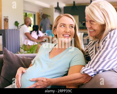 Mère aînée avec fille adulte enceinte assise sur le canapé à la maison ensemble Banque D'Images
