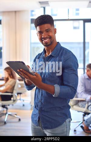 Portrait de Jeune homme d'affaires souriant avec tablette numérique debout et travaillant dans le bureau moderne Banque D'Images