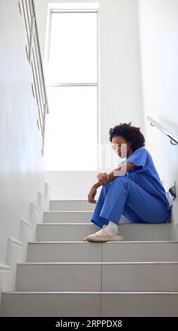 Femme stressée médecin ou infirmière portant des gommages assis sur les escaliers à l'hôpital Banque D'Images