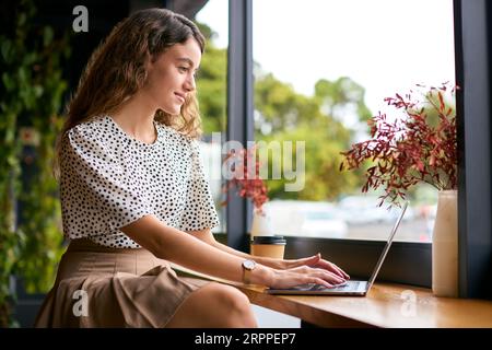 Jeune femme d'affaires avec le café Takeaway travaillant assis sur un ordinateur portable dans un café ou un bureau Banque D'Images