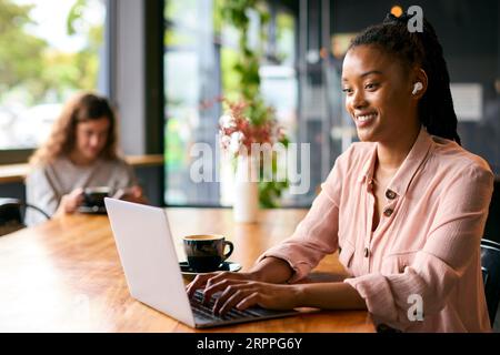 Jeune femme d'affaires portant des écouteurs sans fil travaillant sur un ordinateur portable dans un café ou un bureau Banque D'Images