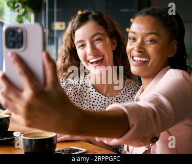 Deux jeunes amies se rencontrent dans le café et posent pour Selfie Banque D'Images