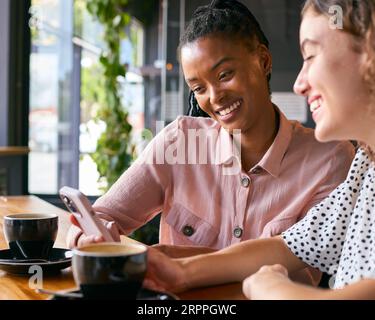 Deux jeunes amies se rencontrent dans le café et regardent le téléphone portable ensemble Banque D'Images