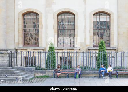 Les touristes font une pause sur un banc à l'extérieur de la bibliothèque Weston, Bodleian Library, Université d'Oxford, Angleterre. Banque D'Images