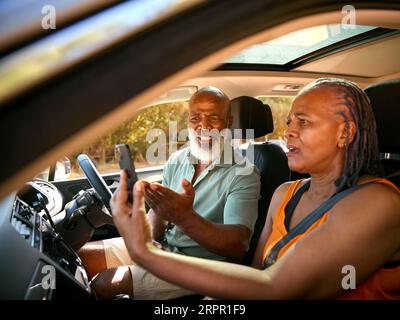 Couple senior en voiture se disputant sur les directions sur GPS Sat Nav sur téléphone portable sur excursion d'une journée Banque D'Images