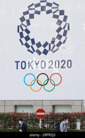 200326 -- PÉKIN, le 26 mars 2020 -- des piétons portant des masques passent devant une affiche de l'emblème de Tokyo 2020 placée devant le bâtiment du gouvernement métropolitain de Tokyo à Tokyo, Japon, le 25 mars 2020. Le ministère de la Santé du Japon et les gouvernements locaux ont déclaré mercredi que 41 nouvelles infections au COVID-19 ont été confirmées à Tokyo, tandis que 66 nouveaux cas ont été confirmés par 12 autres autorités locales, ce qui porte le nombre total de personnes infectées au Japon à 1 277 à 8:00 heures, heure locale ici. PHOTOS XINHUA DU JOUR DuxXiaoyi PUBLICATIONxNOTxINxCHN Banque D'Images