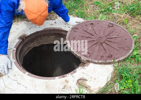 le plombier se pencha sur le puits de béton. Contrôle et entretien des puits septiques. Banque D'Images