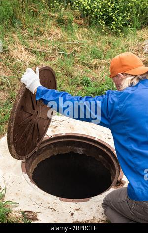 un ouvrier vérifie un puits de plomberie à la campagne. Entretien et nettoyage des puits septiques. Banque D'Images