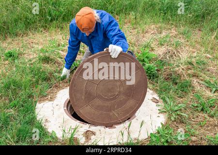 un ouvrier vérifie un puits de plomberie à la campagne. Entretien et nettoyage des puits septiques. Banque D'Images