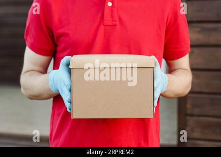 Gros plan du livreur dans la boîte en carton rouge de l'uniforme. Service en quarantaine. Banque D'Images